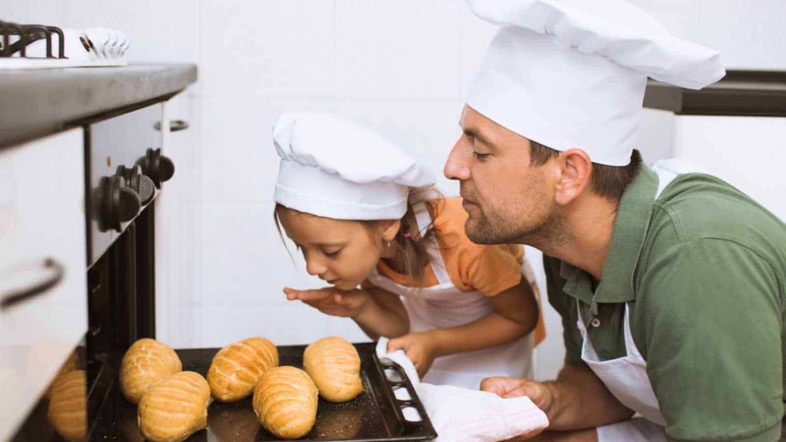 father with daughter take some rolls on a baking tray out of oven