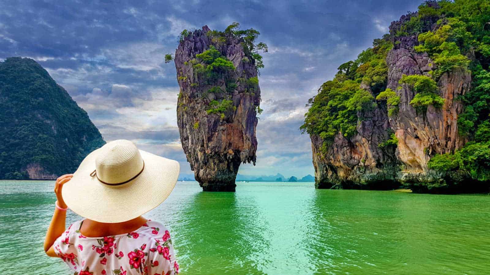Woman tourist with hat and floral dress looking at James Bond island in Thailand