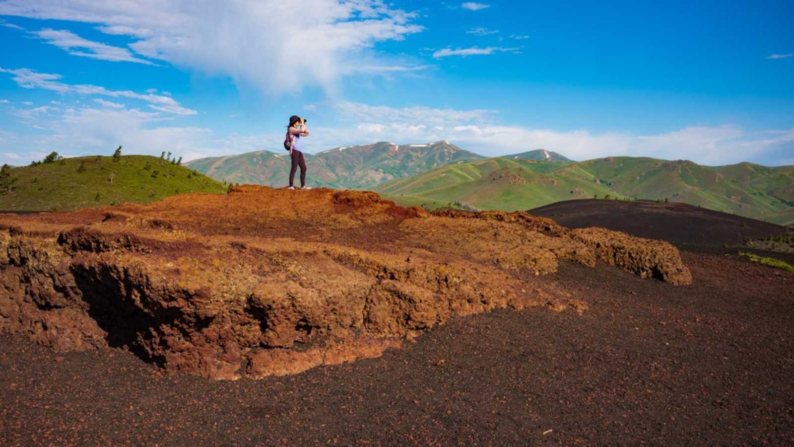 Craters of the Moon National Monument and Preserve, ID, USA - Jun 27, 2022: Rhonda Branca of Binghamton, NY takes in the view of of Big Cider Butte and the Great Rift from the Inferno Cone at sunrise.