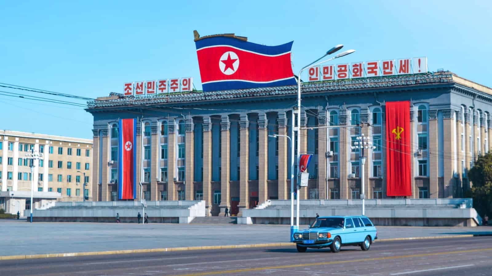 Pyongyang, North Korea - October 9, 2019: Old blue car driving in Pyongyang Street with North Korea Flag
