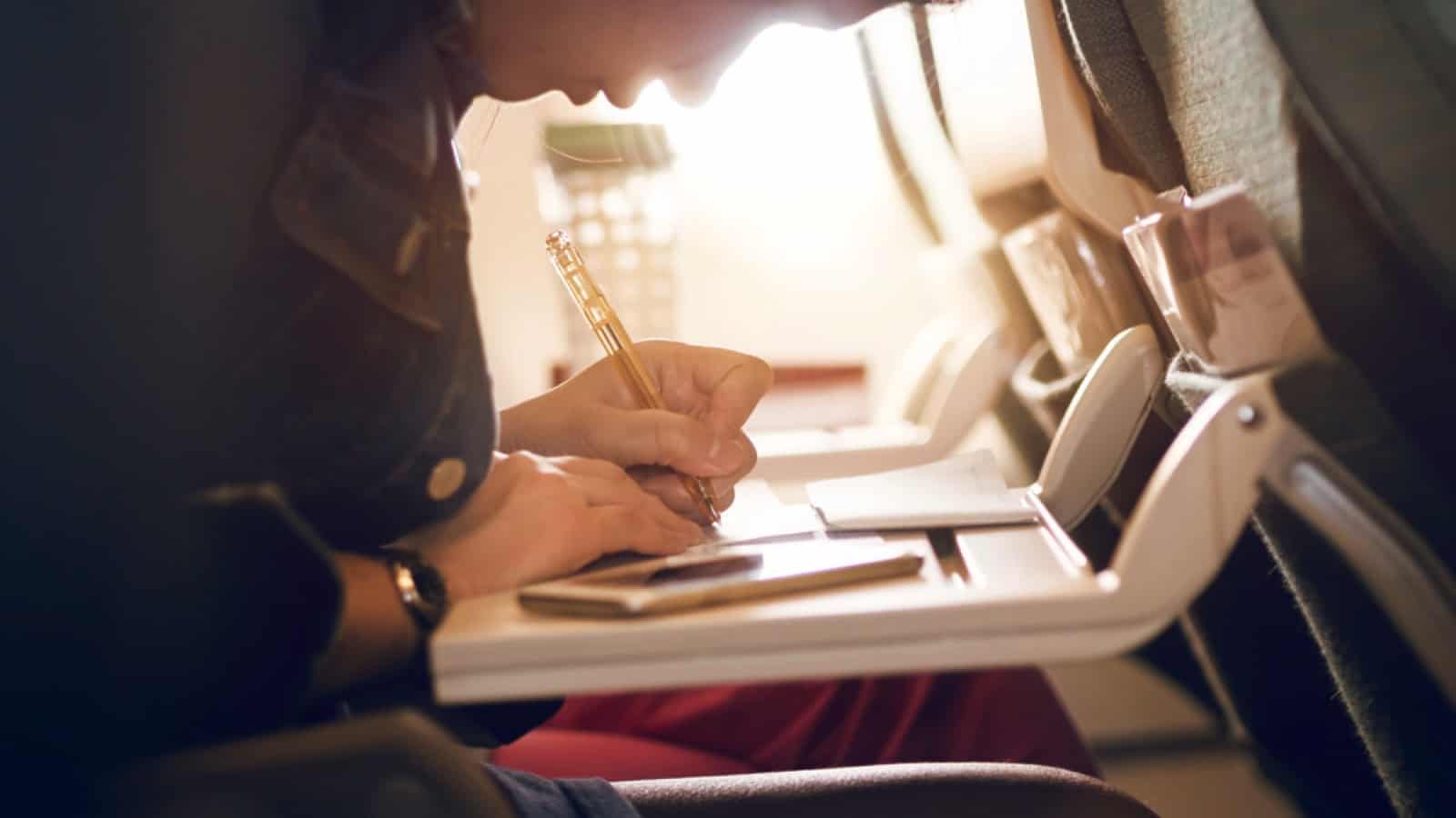 Tourist filling immigration form with pen in flight