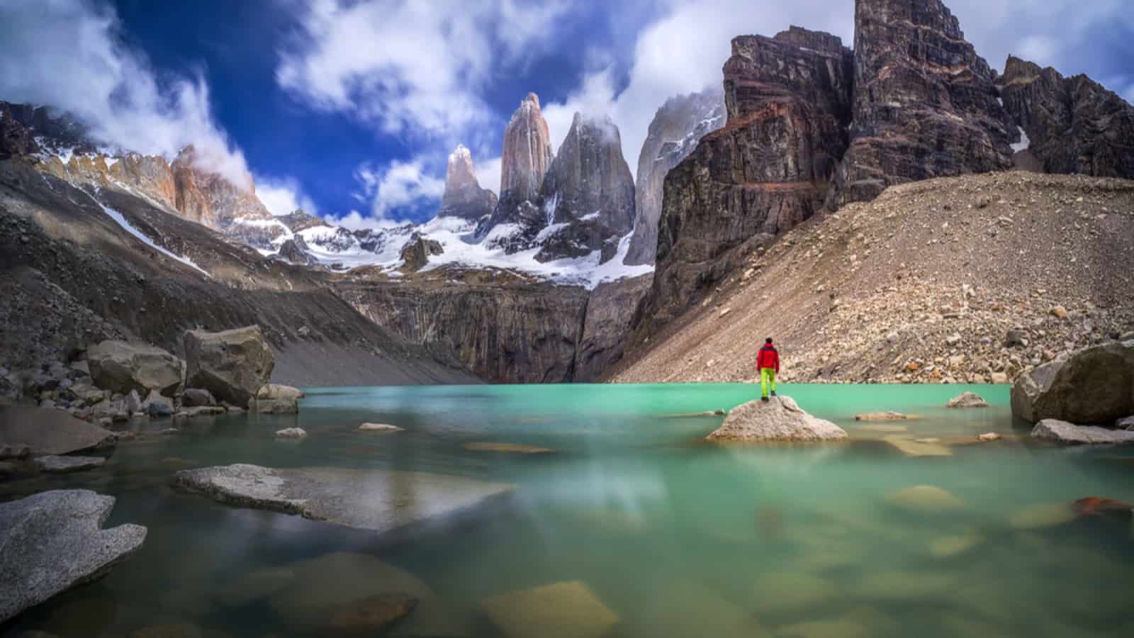 Hiker in red jacket admiring 3 peaks at Base de las Torres viewpoint in Torres del Paine, Patagonia